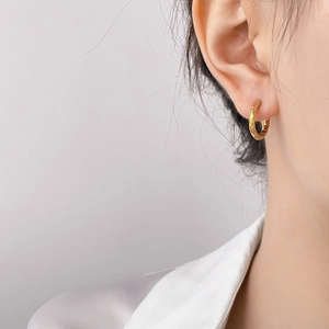 Close-up of golden hammered hoop earring with unique textured finish on a model