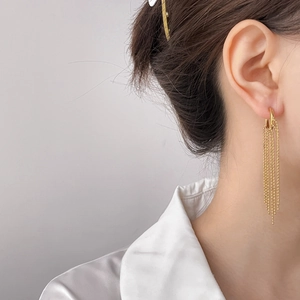 Close-up of gold beaded chain tassel earrings worn with a white satin shirt