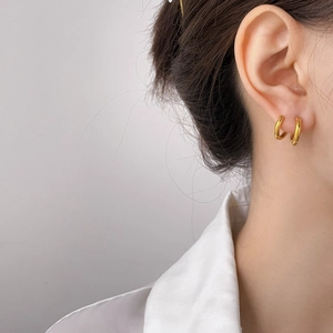 Detail of high-polished gold double hoop earrings worn by a model in minimalist style