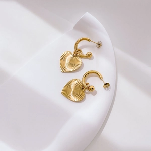 Detail of gold heart earrings with radiant sunburst texture on a minimalist background