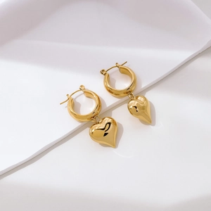 Macro view of gold hoop earrings with polished heart pendants and zircon details