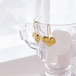 Macro shot of gold heart dangle earrings hanging on a vintage crystal glass rim