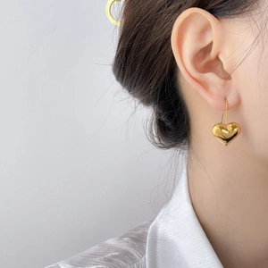 Detailed close-up of golden hollow heart drop earrings on a model with polished finish