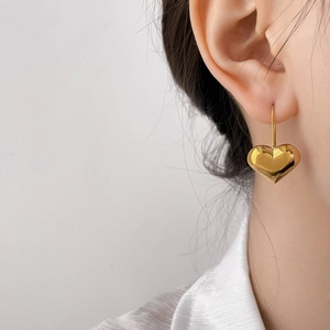Close-up of golden hollow heart earrings with polished finish on model ear