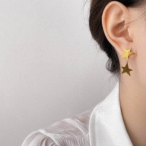 Close-up of a model wearing double layered gold star stud earrings with a polished finish