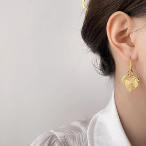 Detailed view of heart-shaped gold drop earrings with textured finish on model