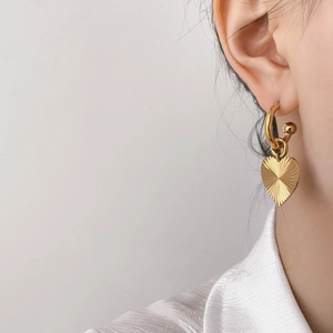 Elegant gold heart hoop earrings with sunburst texture shown on a model's ear