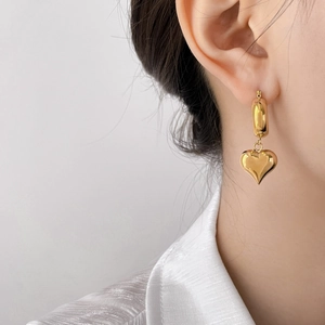 Close-up of model wearing gold hollow heart-shaped dangle earrings with polished finish
