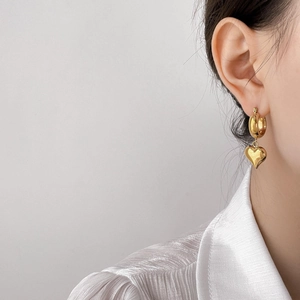 Elegant gold heart charm hoop earrings with polished finish on model in silk shirt