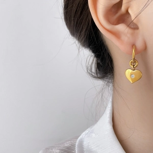 Close-up of golden heart-shaped earrings with zircon inlay worn by a model