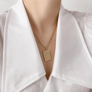 Close-up of golden checkerboard square pendant necklace on model with white shirt