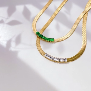 Detailed shot of 18K gold snake chain necklaces with emerald and clear zircon inlay