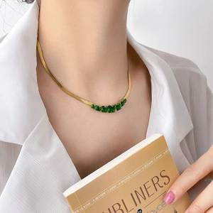 Detailed view of gold herringbone necklace featuring five emerald green square stones