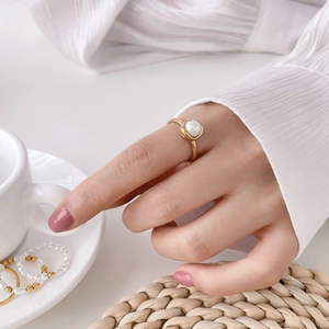 Gros plan d'une bague perle dorée à l'or 18 carats portée par un mannequin en extérieur