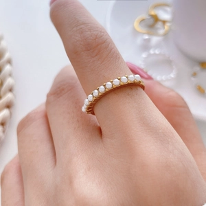 Détail d'une bague en acier plaqué or 18K avec une rangée de perles blanches élégantes
