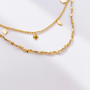 Detail of layered gold snake chain necklace featuring a geometric rhombus pendant