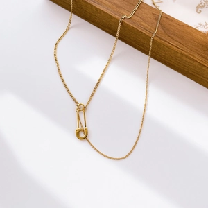 Macro detail of gold layered necklace featuring a minimalist safety pin moon pendant