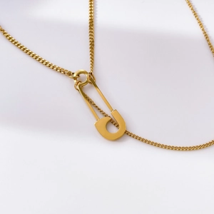 Detail of a minimalist gold safety pin pendant on a fine snake chain necklace