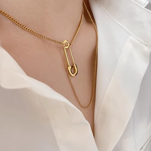 Elegant gold safety pin pendant necklace with layered chain detail worn on a model