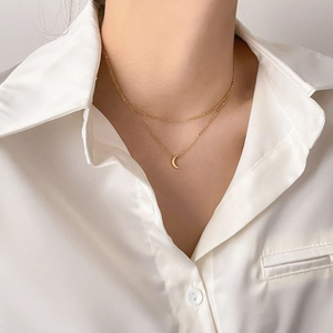 Detail of a layered gold necklace with a mini crescent moon pendant on a white shirt