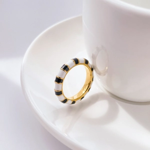 Detailed shot of gold ring featuring black and white enamel stripes on a ceramic saucer