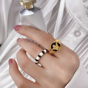 Macro detail of gold angel relief seal ring paired with black and white enamel stripe band