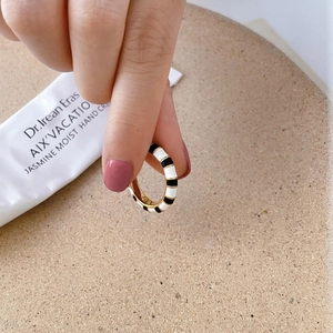 Detail view of a gold ring with black and white enamel stripes held by hand