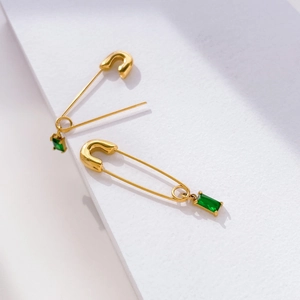 Detailed view of gold safety pin earrings with hanging emerald green rectangle zircons