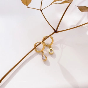 Detail of gold hoop earrings with green drop-shaped zircon hanging on a wooden branch