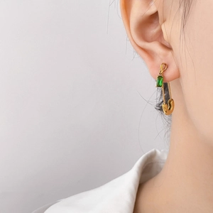 Elegant gold safety pin earrings featuring an oval green zircon gemstone on model