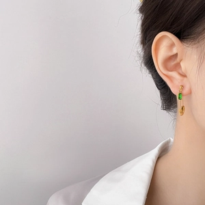 Detail view of a gold safety pin earring featuring a sparkling emerald green zircon stone