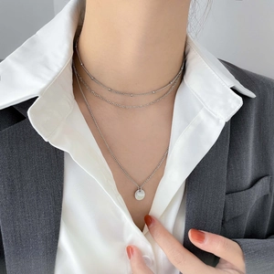 Gros plan d'un collier multicouche argenté avec pendentif rond porté par un mannequin