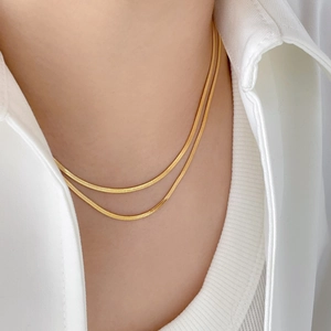 Détail de colliers superposés en maille serpent dorée portés sur un col blanc