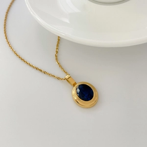 Detailed close-up of a gold oval pendant featuring a deep blue sapphire gemstone