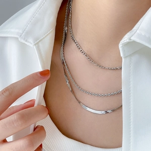 Détail de colliers argentés superposés avec chaînes Figaro, corde et serpent plat au cou