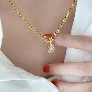 Golden Cuban chain necklace with oval sapphire pendant worn on model with white shirt
