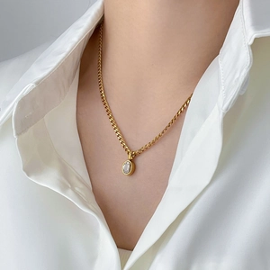Close-up of a gold oval sapphire pendant necklace worn by a model on a white shirt