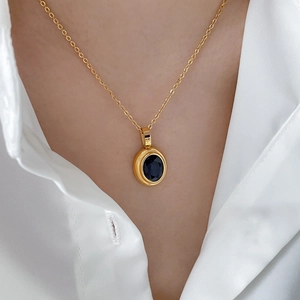 Detail of an oval sapphire pendant on a gold chain worn over a white collared shirt