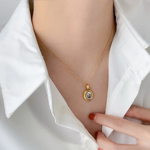 Close-up of gold oval necklace with clear zircon pendant worn on a white shirt