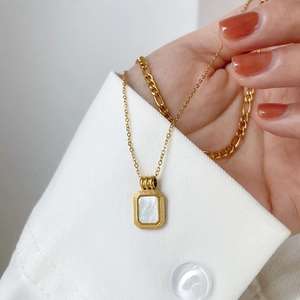 Nahaufnahme einer zweilagigen Goldkette mit quadratischem weißem Muschelanhänger auf Hemd