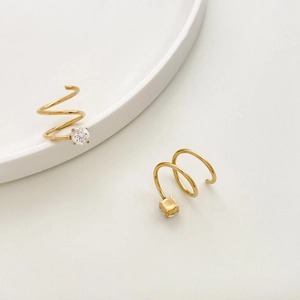 Macro detail of gold spiral earrings with zircon stone on white ceramic dish surface