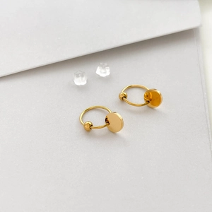 Detail of gold circular earrings with round charms and silicone backs on white paper