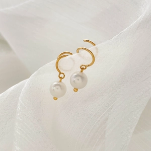 Close-up of gold hoop earrings featuring polished white pearls on delicate white mesh fabric