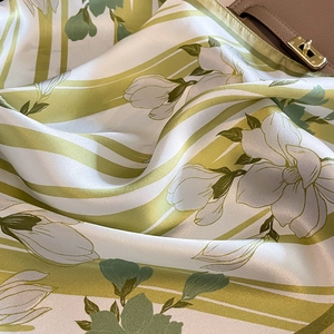 Pañuelo de seda verde y blanco con estampado de magnolia sobre un bolso de piel de lujo