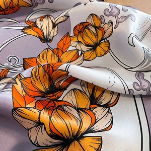 Macro detail of silk scarf showing vibrant orange magnolia print and glossy satin texture