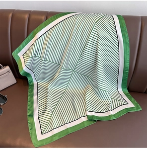 Élégant foulard carré en soie à rayures vertes et blanches posé sur un canapé en cuir