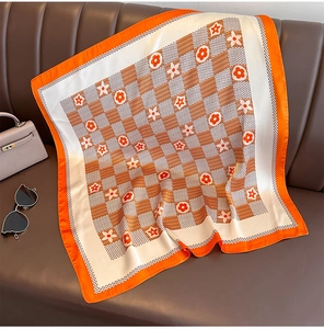 Détail d'un foulard en soie à carreaux orange et fleurs sur fond en cuir marron
