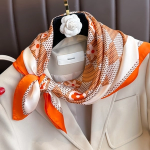 Carré de soie à imprimé floral orange et blanc élégamment noué sur un col de blazer beige