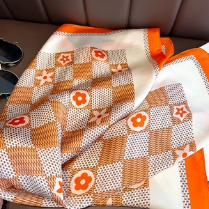 Détail du motif floral à damier orange sur le foulard en soie posé sur du cuir