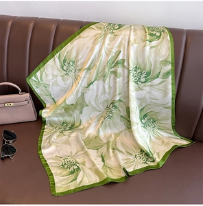 Detailed view of elegant green floral silk scarf draped on a vintage leather sofa